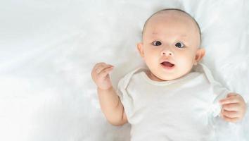 famille heureuse, mignon petit garçon nouveau-né asiatique allongé jouer sur un lit blanc regarder la caméra avec un sourire riant visage heureux. petit nouveau bébé adorable enfant innocent au premier jour de la vie. notion de fête des mères. photo