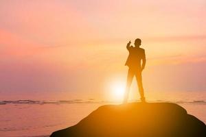 silhouette d'homme d'affaires ingénieur célébration succès bonheur sur un ciel de soirée en pierre coucher de soleil sur fond de plage, sport et concept de vie active. photo