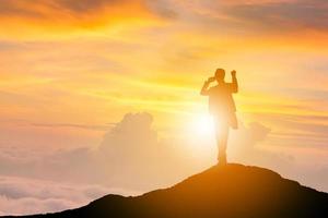 silhouette d'homme d'affaires célébration succès bonheur sur fond de ciel de soirée au coucher du soleil au sommet d'une montagne, sport et concept de vie active, avec un tracé de détourage. photo