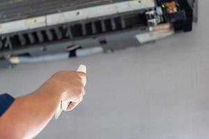 un technicien masculin allume le climatiseur avec télécommande, un technicien masculin fixe et nettoie un climatiseur moderne à l'intérieur, des concepts d'entretien et de réparation photo