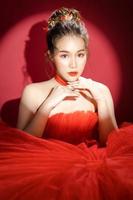 jeune modèle de jolie femme asiatique dans une robe rouge de luxe élégante et chic sur fond rouge isolé.