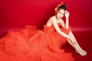 jeune modèle de jolie femme asiatique dans une robe rouge de luxe élégante et chic sur fond rouge isolé. photo