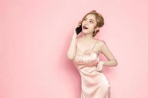 portrait joyeuse jolie jeune femme asiatique excitée tenant un smartphone dans sa main sur fond rose. grande offre mobile, consumérisme, concept de style de vie. photo