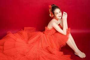 jeune modèle de jolie femme asiatique dans une robe rouge de luxe élégante et chic sur fond rouge isolé. photo