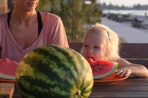 une mère avec deux enfants mange des tranches de pastèque à l'extérieur en été photo