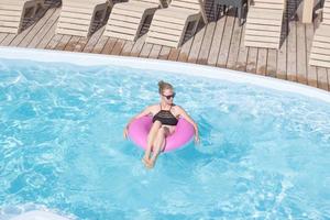 jeune femme blonde se relaxant dans la piscine bleue, vacances d'été photo