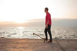 patineur avec sac à dos regardant le lever ou le coucher du soleil dans la mer ou l'océan photo