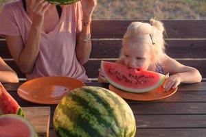 une mère avec deux enfants mange des tranches de pastèque à l'extérieur en été photo