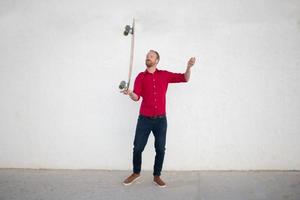 jeune homme barbu à cheval sur planche à roulettes, hipster avec longboard en chemise rouge et fond urbain de jeans bleus photo