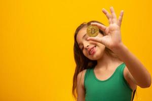 enfant tenant une crypto-monnaie en métal. Pièce d'or. d'or. sur fond jaune. photo