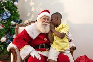 petit garçon africain chuchotant à l'oreille du père noël. dire un secret. dévoilant le cadeau que vous aimeriez gagner. parler de la façon dont elle s'est comportée pendant l'année. photo