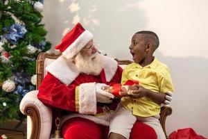 le père noël offrant une boîte-cadeau à un petit garçon africain. réveillon de noël, livraison de cadeaux. photo