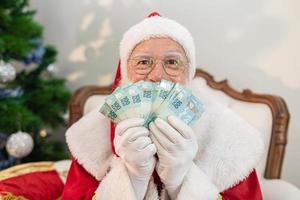 le père noël compte les billets d'argent brésiliens. vraies notes. Billets de 100 reais. concept d'épargne pour la fin de l'année. dépenser à Noël. dépensés en cadeaux de Noël. photo