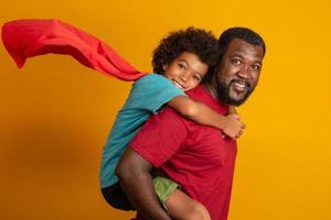 père et fils africains jouant au super-héros pendant la journée. les gens s'amusent sur fond jaune. concept de famille amicale. photo