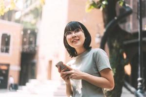 une jeune femme asiatique heureuse adulte porte des lunettes à l'aide d'un téléphone portable pour les médias sociaux.