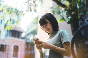 une jeune femme asiatique adulte porte des lunettes en utilisant le commerce de téléphonie mobile crypto cion et nft pour un profit d'argent avec un graphique numérique. photo