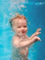 mignon souriant adorable bébé fille plongeant dans la piscine bleue sous-marine. mode de vie actif, cours de natation pour enfants. activité de sports nautiques pendant les vacances d'été en famille dans un complexe tropical photo