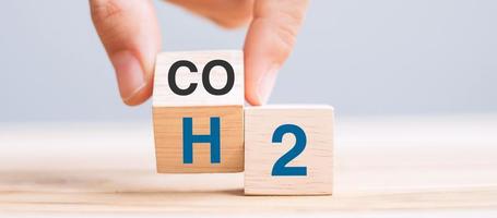 Retourner à la main des blocs de cube en bois avec du dioxyde de carbone co2, passer au texte d'hydrogène h2 sur fond de table. concepts de carbone libre, d'énergie alternative et de changement climatique mondial photo