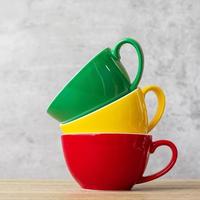 pile de tasses à café colorées sur fond de mur au café. tasse en céramique de couleur verte, jaune et rouge sur la table à la maison. concept de la journée internationale du café photo