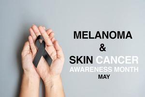 mélanome et cancer de la peau, mois de sensibilisation aux blessures causées par les vaccins et concepts de repos en paix. homme tenant un ruban noir sur fond gris photo