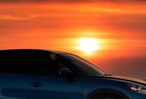 vue latérale d'une voiture suv bleue au design sportif et moderne garée sur une route en béton au bord de la plage au coucher du soleil. technologie de la voiture électrique. voyage en voiture. industrie automobile. ciel coucher de soleil rouge et jaune. photo