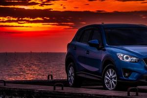 voiture suv compacte bleue au design sportif et moderne garée sur une route en béton au bord de la mer au coucher du soleil le soir. concept de technologie de voiture hybride et électrique. place de parking. industrie automobile. photo