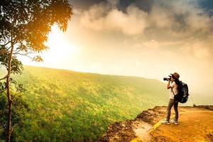 jeune femme voyageant avec sac à dos, chapeau et support de caméra sur la falaise de la montagne. femme photographe prenant des photos de la forêt tropicale, du ciel et des nuages pendant ses vacances. une femme asiatique voyage seule.