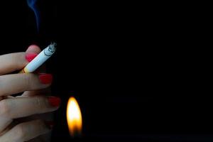 femme sexy avec un ongle rouge fume une cigarette sur fond sombre avec espace de copie. arrêter de fumer. cigarette brûlant avec la flamme du briquet. accro à la nicotine. 31 mai journée mondiale sans tabac. photo