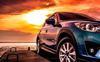 voiture suv bleue au design sportif et moderne garée sur une route en béton à la plage de la mer au coucher du soleil avec un ciel orange. concept de technologie de voiture hybride et électrique. industrie automobile. fond d'écran de service d'entretien de voiture. photo