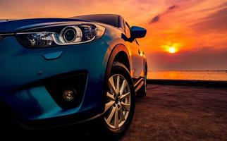 voiture suv de luxe garée sur un parking près de la plage au coucher du soleil. vue de face de la nouvelle voiture suv avec un design sportif et moderne et un beau ciel doré au coucher du soleil. voyage sur la route pendant les vacances d'été. véhicule électrique. photo