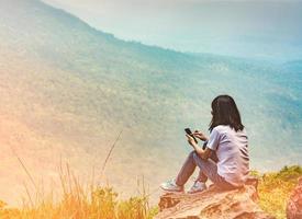 une jeune femme asiatique s'assoit sur le rocher à la falaise et utilise un message de téléphone intelligent à ses amis pendant ses vacances dans le parc national. concept de voyage d'aventure et de communication photo