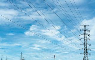 pylône électrique haute tension et fil électrique contre le ciel bleu et les nuages. vue de dessous du pylône électrique. tour de réseau haute tension avec câble métallique. lignes de transmission sur la tour du réseau haute tension. photo