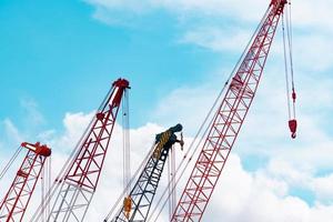 grue sur chenilles contre le ciel bleu et les nuages blancs. secteur immobilier. la grue sur chenilles rouge utilise un équipement de levage de bobine sur le chantier de construction. grue à louer. concessionnaire de grues pour les entreprises de construction. photo