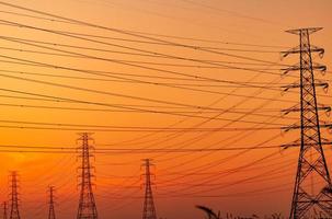 silhouette pylône électrique haute tension et fil électrique avec un ciel orange. poteaux électriques au coucher du soleil. concept de puissance et d'énergie. tour de réseau haute tension avec câble métallique à la station de distribution. photo