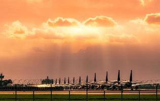 avion commercial stationné sur le parking de l'aéroport après l'impact de la crise du coronavirus sur les activités aéronautiques. l'avion est garé à l'intérieur de la clôture de l'aéroport avec un ciel coucher de soleil et un champ d'herbe verte. photo