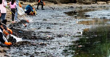 bénévoles adultes et enfants ramassant les ordures sur la plage de la mer. pollution de l'environnement de la plage. ranger les ordures sur la plage. les gens portent des gants orange pour ramasser les ordures dans un sac en plastique. photo