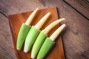 maïs miniature sur planche à découper en bois, jeune maïs frais pour la cuisson d'aliments santé, gros plan maïs biologique brut sur fond de bois. photo