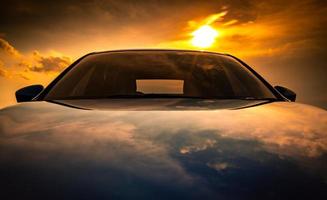 voiture suv compacte bleue au design sport, moderne et luxueux garée sur une route en béton au bord de la mer au coucher du soleil. vue de face d'une belle voiture hybride sur fond orange ciel et nuages. voyager en vacances photo