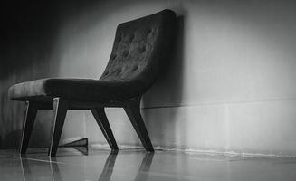 chaise classique noire au design unique dans une salle de repos vide près d'un mur de béton sur fond sombre et dramatique. concept déprimé, triste et solitaire. un fauteuil vide dans le salon. mobilier d'intérieur. photo