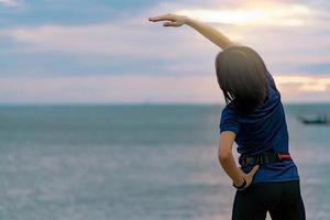 séance d'entraînement de femme silhouette le matin à la plage de pierre avec un beau ciel de lever de soleil. fit woman runner qui s'étend du corps avant de courir. exercice cardio pour un mode de vie sain. séance d'entraînement de fille active seule. photo