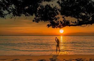 silhouette vue arrière d'une femme sexy regardant le beau coucher de soleil sur la plage paradisiaque tropicale. une fille heureuse porte un bikini et un chapeau de paille relaxant des vacances d'été. voyage de vacances. ambiance estivale. une vie paisible. photo