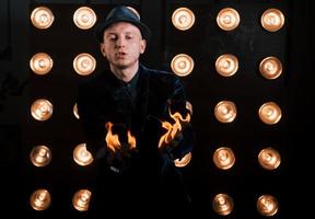 bien brûlant. illusionniste professionnel en chapeau noir, chemise et gants jouant avec le feu photo