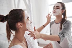 qui a besoin d'un maquilleur quand vous avez un ami. conception de soins de la peau en utilisant un masque blanc sur le visage. deux soeurs ont un week-end dans la chambre photo