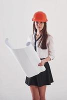 attention pour cette tâche. femme brune en jupe et casque de couleur orange avec du papier dans les mains se dresse sur fond blanc dans le studio photo