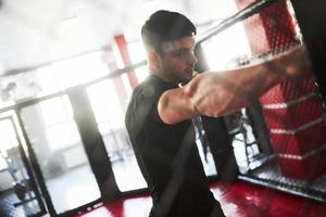 la lumière du jour vient des fenêtres derrière. un homme fort boxe dans la salle de gym derrière la clôture. fait de l'exercice quotidiennement photo