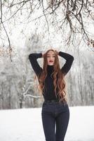 mains sur la tête. jolie fille aux cheveux longs et en chemisier noir est dans la forêt d'hiver photo