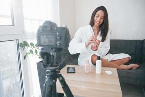 devant la caméra sur le trépied. conception de la mode et des soins de la peau. fille brune utilise des cosmétiques photo