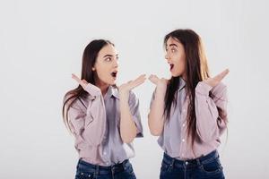 ne peux pas croire. Deux soeurs jumelles debout et posant dans le studio avec un fond blanc photo