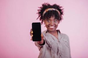 photo centrée. tenant un téléphone noir à la main. jolie femme afro-américaine en vêtements décontractés sur fond rose dans le studio