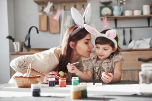 femme donne un baiser. mère et fille dans des oreilles de lapin à Pâques s'amusent dans la cuisine pendant la journée photo